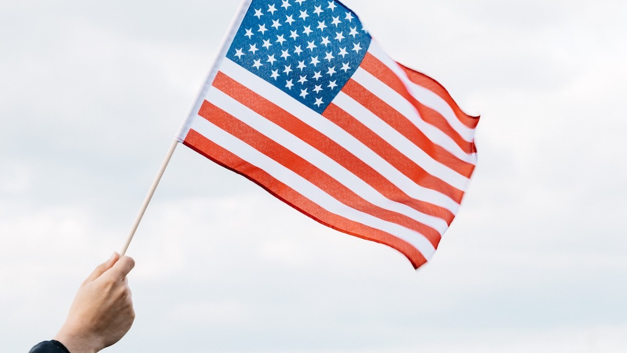 Crop faceless person raising flag of USA above green lawn | Veteran Car Donations
