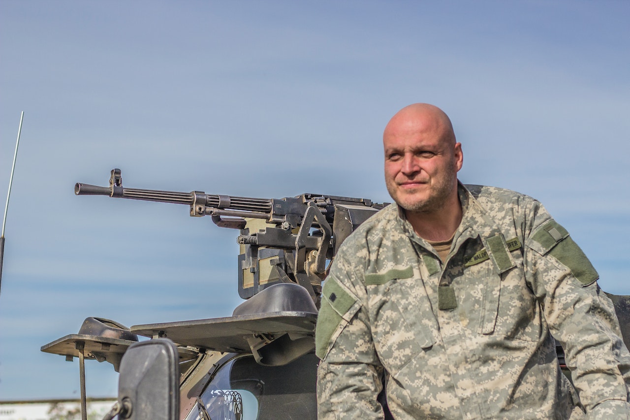 Man in US Army Uniform Siting next to Machine Gun Mounted on top | Veteran Car Donations