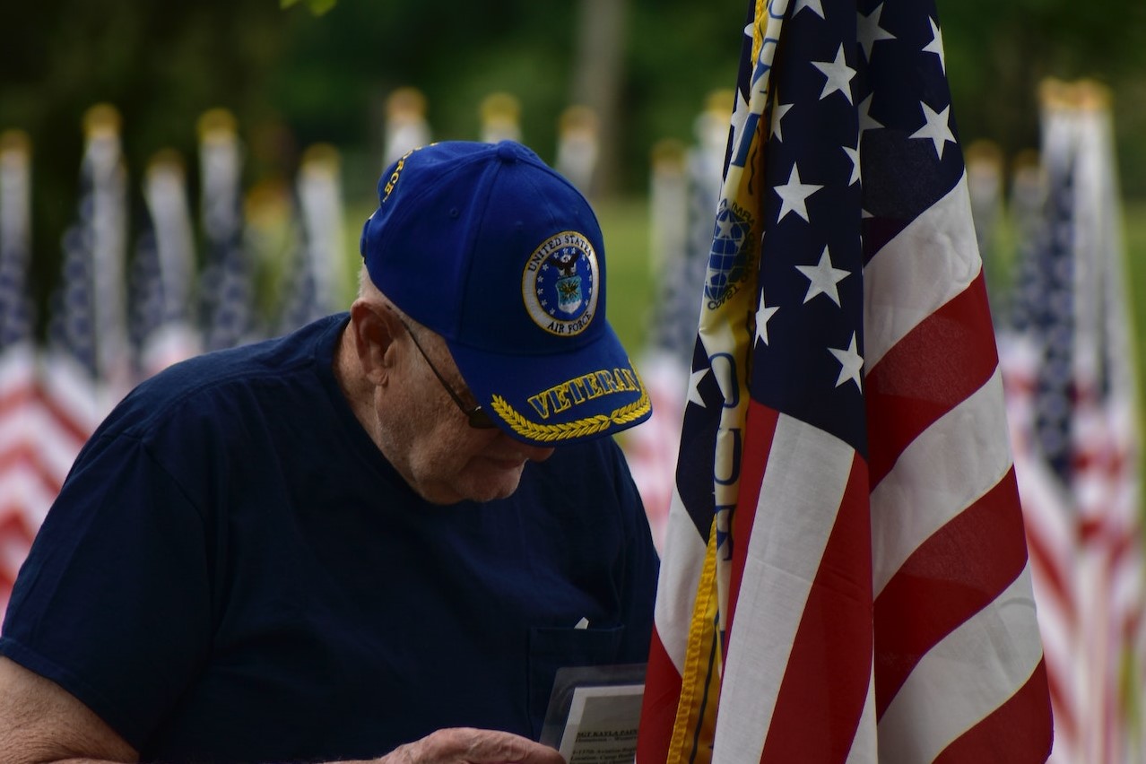 An Elderly Man Standing Beside an American Flag | Veteran Car Donations