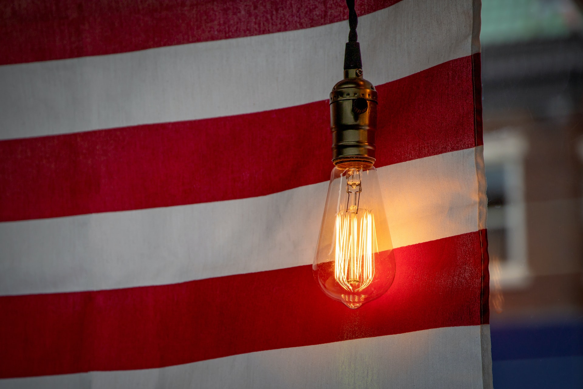 Edison bulb shines a light of hope in front of "Old Glory," the flag of the United States of America in a 4th of July window display | Veteran Car Donations