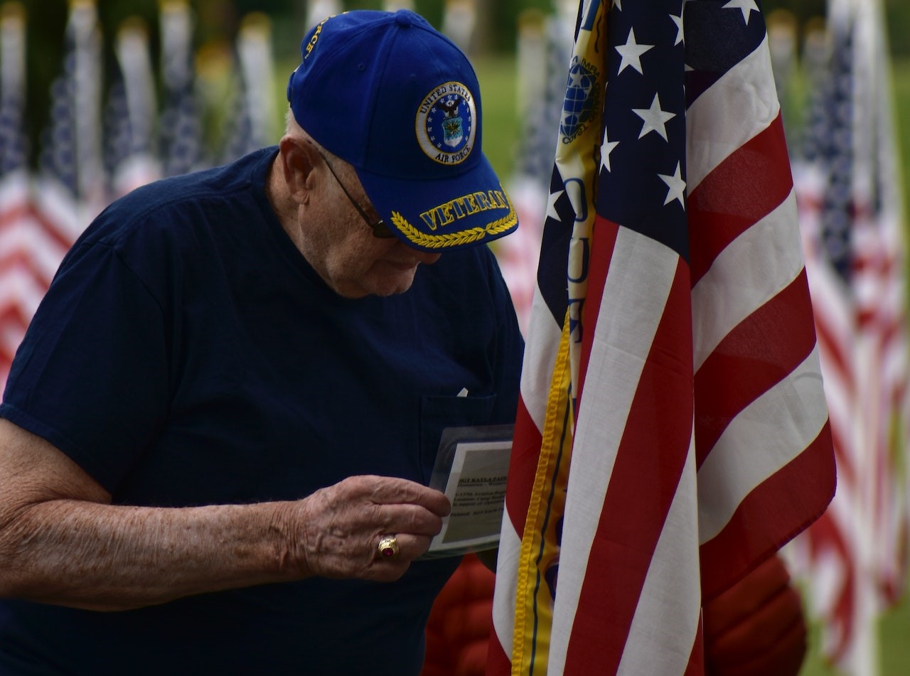 An Elderly Man Standing Beside an American Flag | Veteran Car Donations