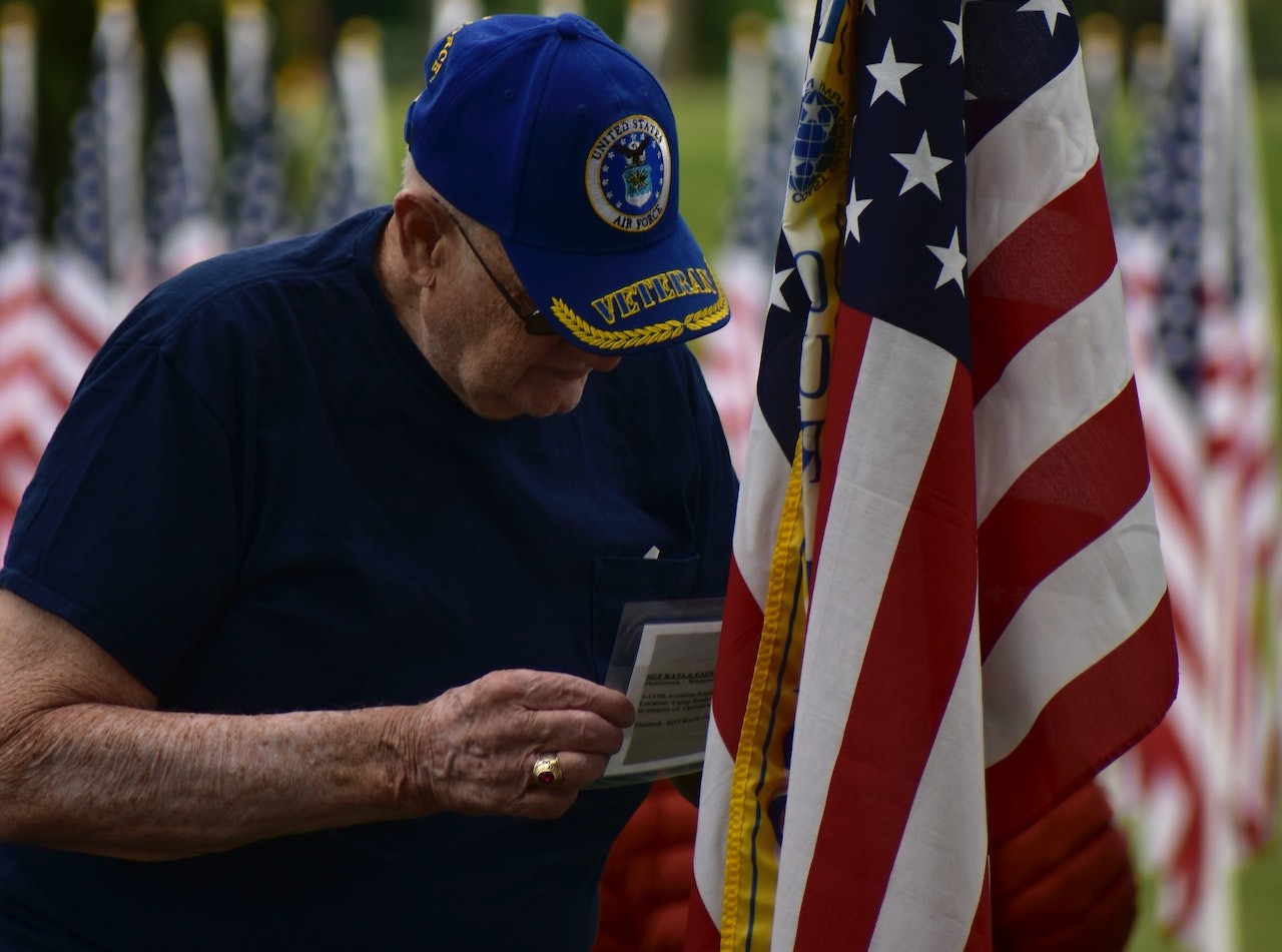 An Elderly Man Standing Beside an American Flag | Veteran Car Donations
