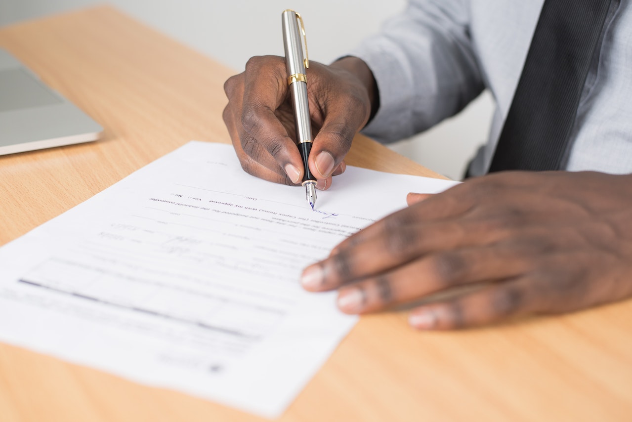 Person Holding Gray Twist Pen and White Printer Paper on Brown Wooden Table | Veteran Car Donations