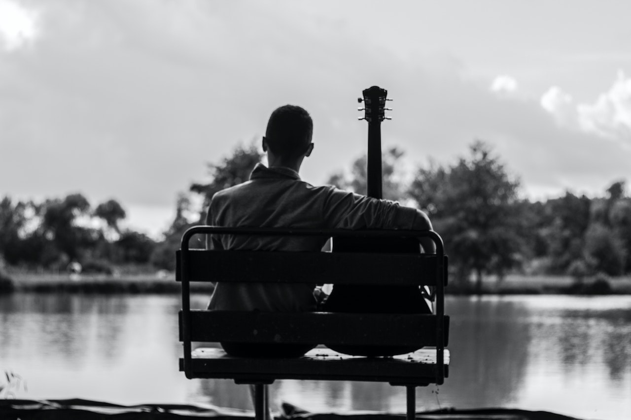 Grayscale Photo of Man Sitting Beside Guitar | Veteran car Donations
