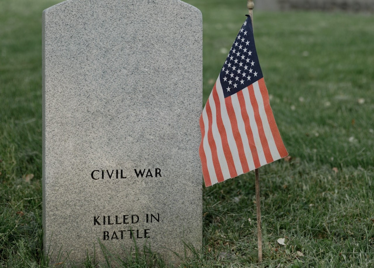 American Flag Beside a Gray Tombstone Of A Veteran | Veteran Car Donations
