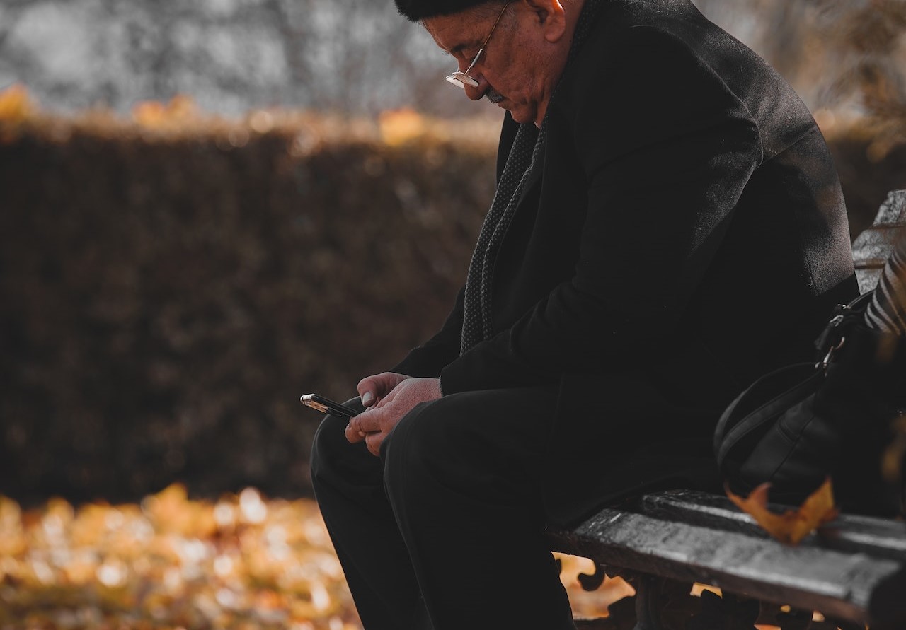 Photo of Man Sitting on Wooden Bench While Using Cellphone | Veteran Car Donations
