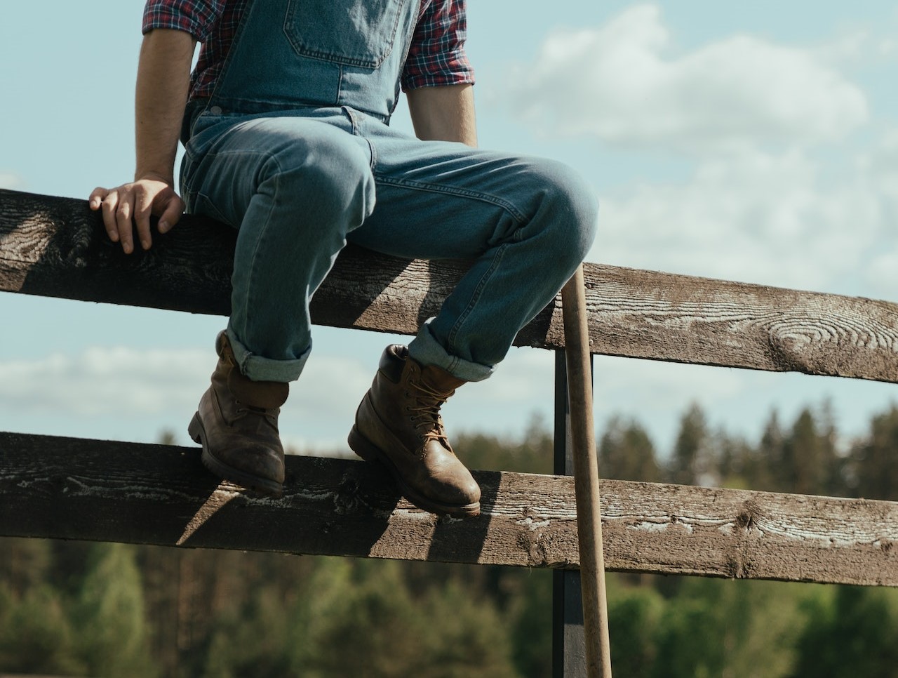 Person in Blue Denim Jeans and Brown Boots Sitting on Brown Wooden Fence | Veteran Car Donations