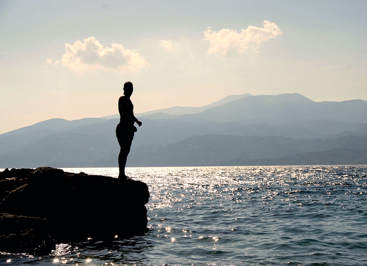 Person Standing on Rock Besides Sea Near Island during Daytime | Veteran Car Donations