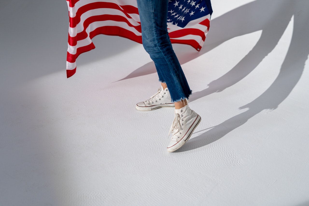 Person in Blue Denim Jeans and White Sneakers Standing Beside Us Flag | Veteran Car Donations
