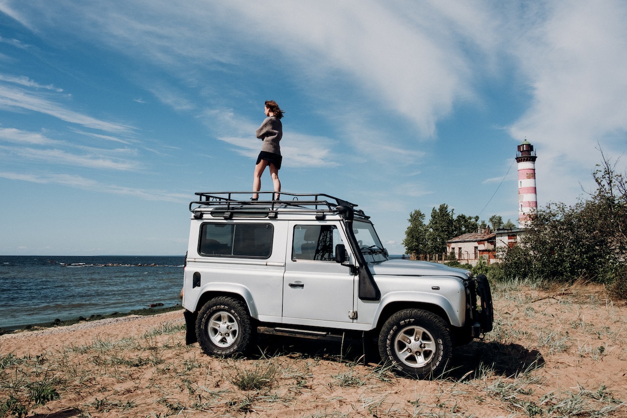 A Woman Standing on White Suv on Beach | Veteran Car Donations