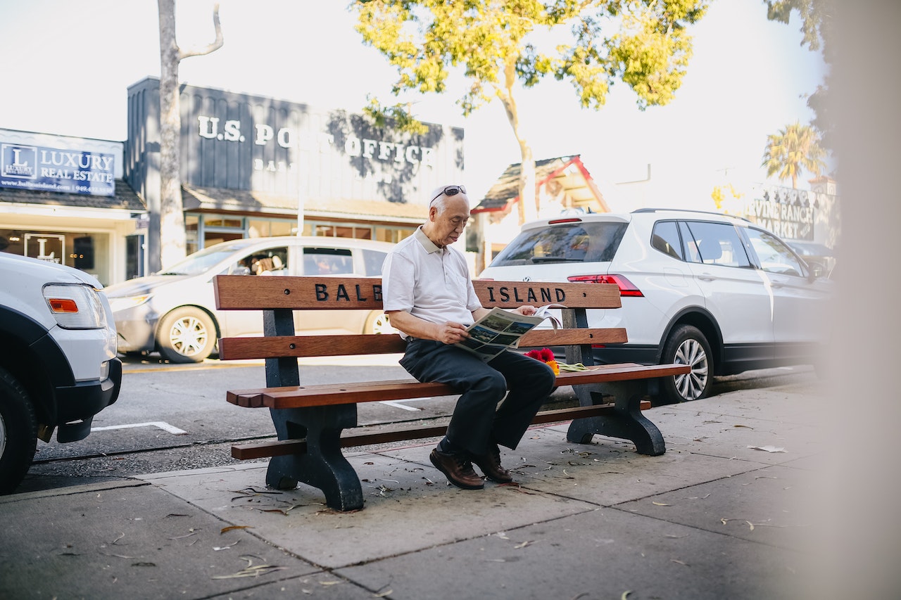 Elderly Man Sitting on the Bench Reading a Newspaper | Veteran Car Donations
