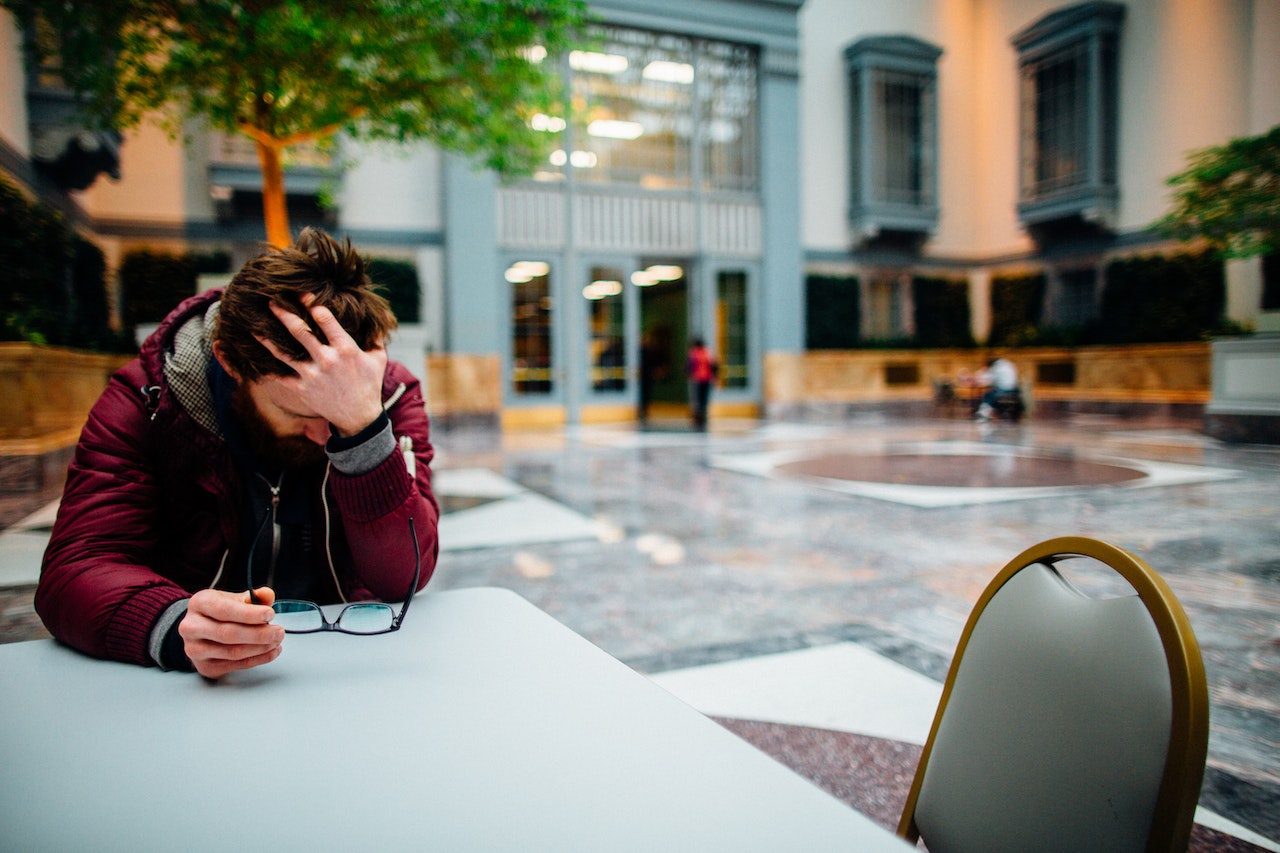 Selective Focus Photography of a Man Holding His Head and Eyeglasses Sitting Beside a Table | Veteran Car Donations