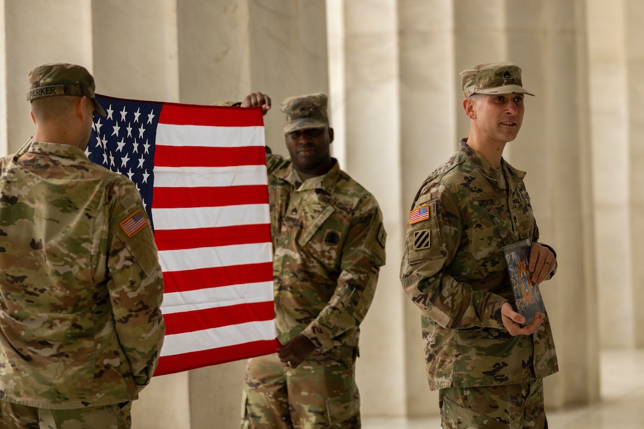 Man in Green Camouflage Uniform Holding a US Flag | Veteran Car Donations
