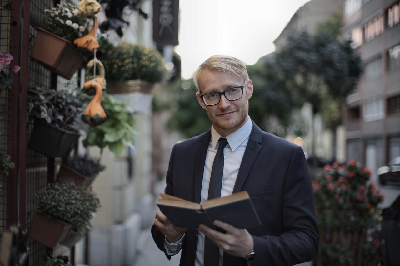 Smiling bearded man in formal wear reading book in street | Veteran Car Donations