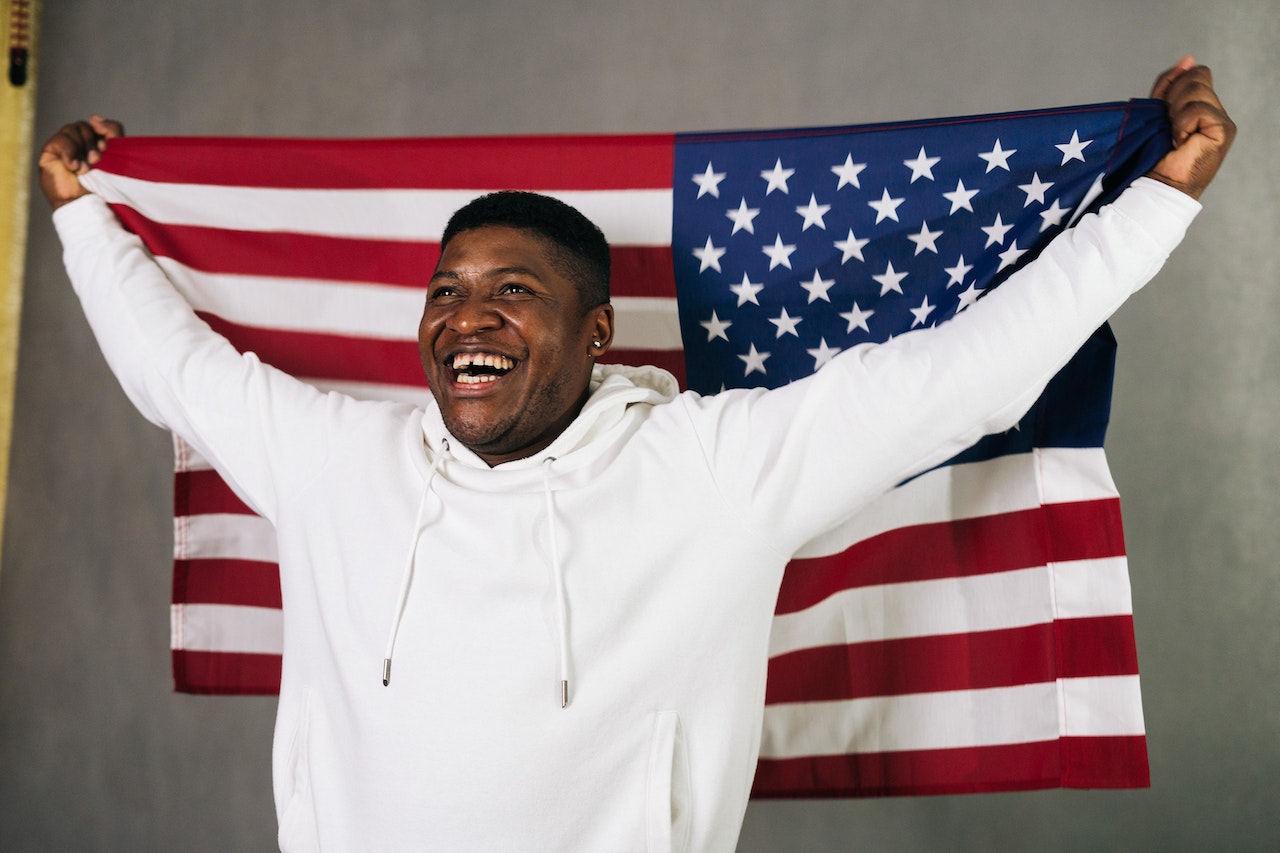 Close-Up Photo of a Man in a White Hoodie Holding a United States of America Flag | Veteran Car Donations