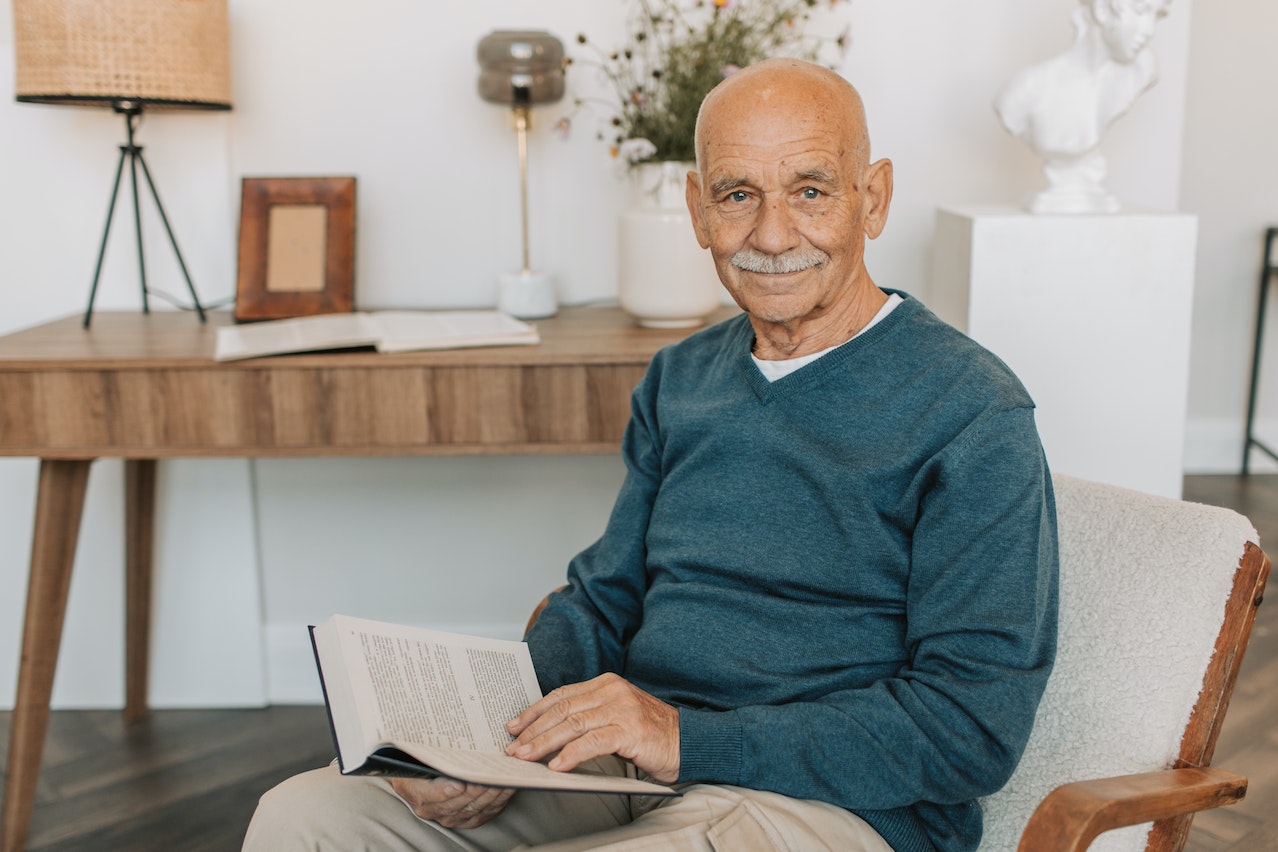 Elderly Man in Blue Sweater Holding a Book | Veteran Car Donations

