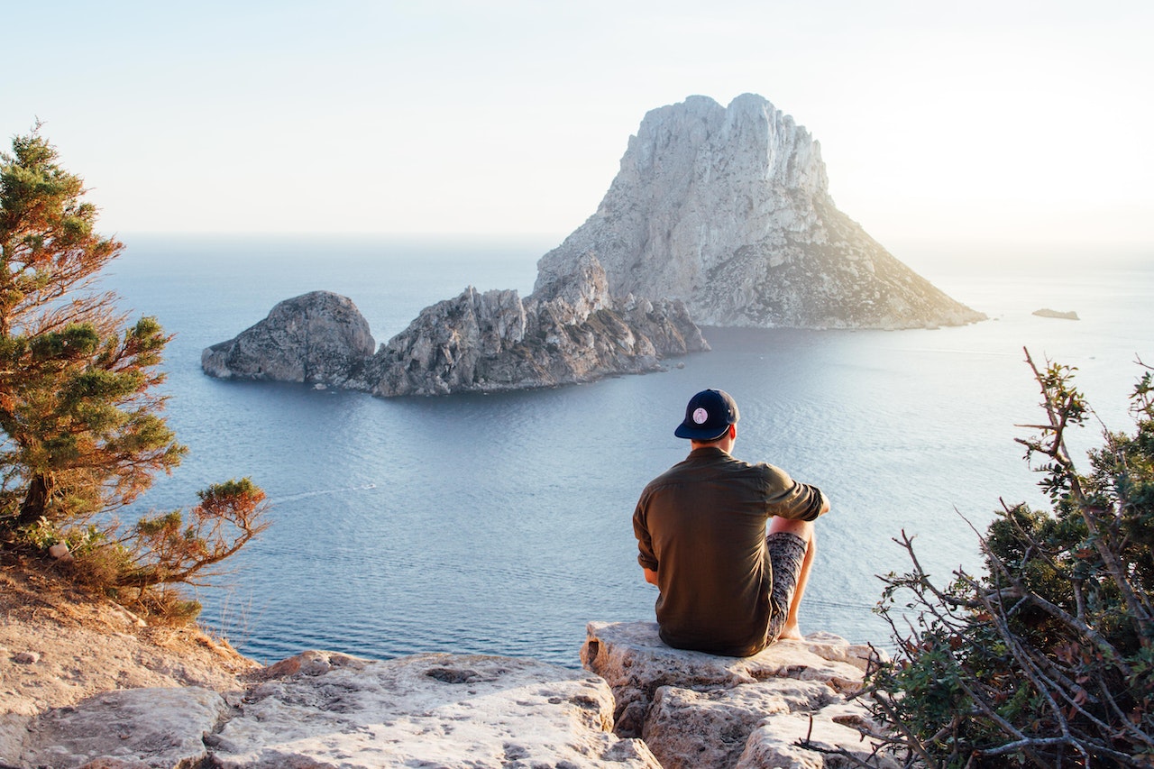 Rear View of Man Sitting on Rock by Sea | Veteran Car Donations
