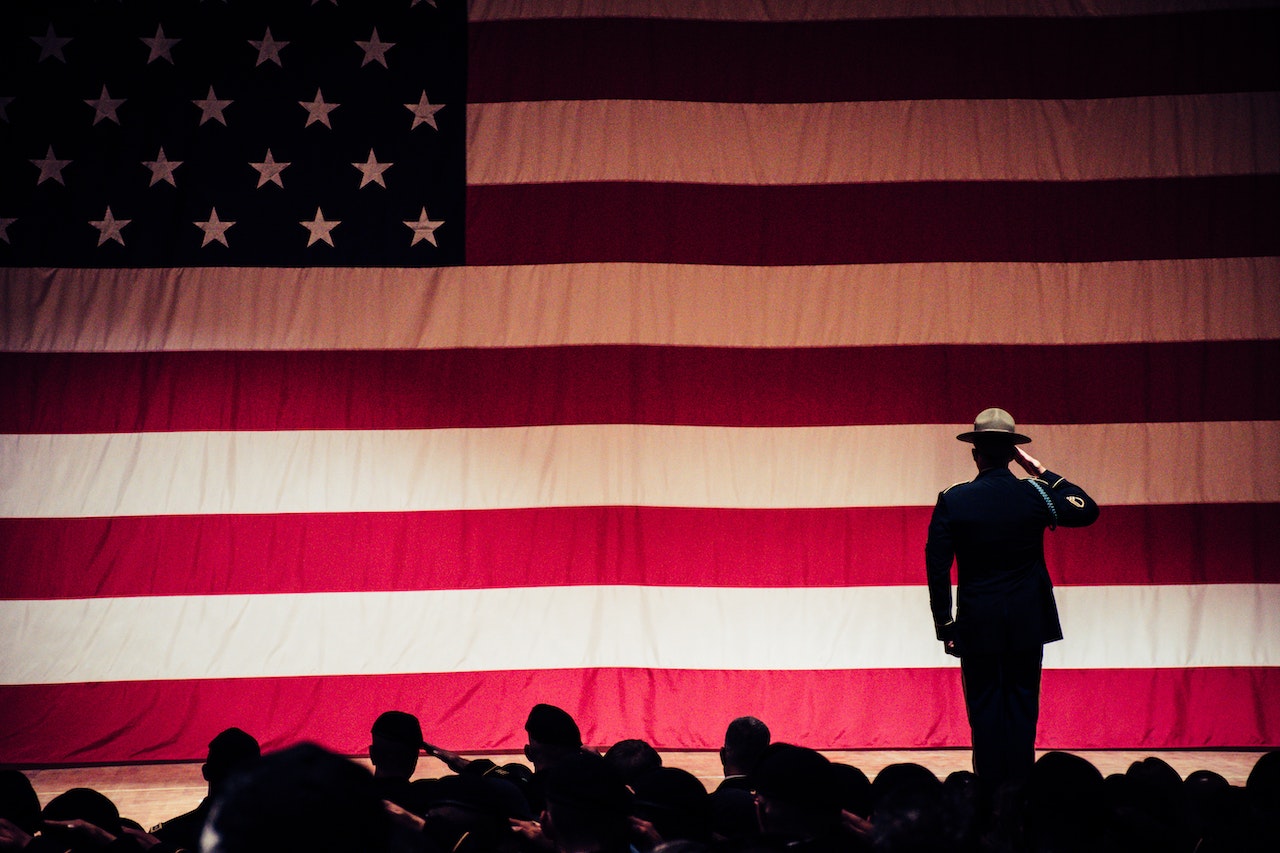 Man Standing On Stage Facing An American Flag | Veteran Car Donations