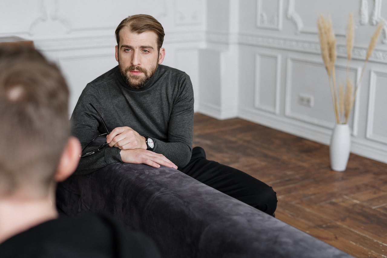 Man in Gray Sweater Sitting on Black Couch | Veteran Car Donations
