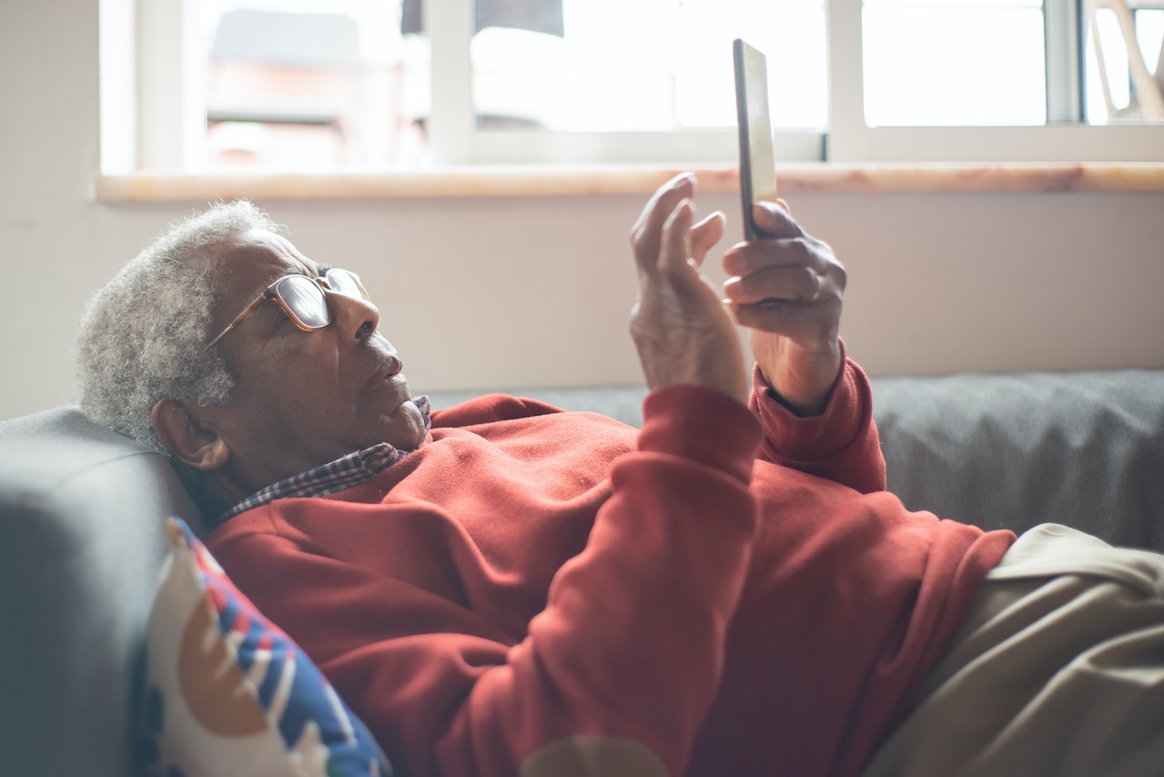 An Elderly Man Using a Cellphone while Lying Down on a Couch | Veteran Car Donations
