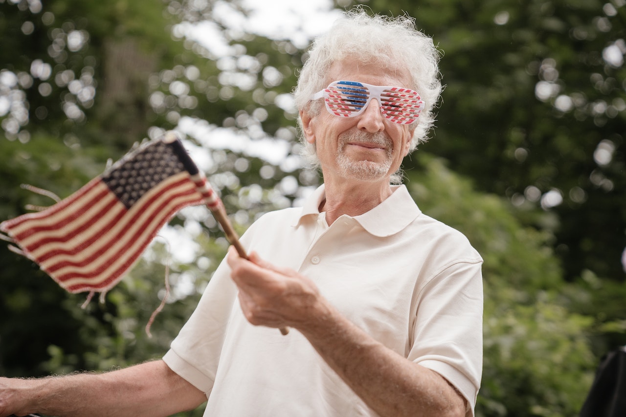 An Elderly Man in White Polo Shirt Holding an American Flaglet | Veteran Car Donations