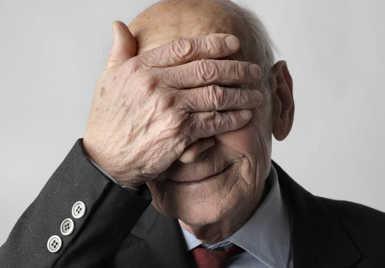 Elderly Man in Black Suit Jacket Covering His Eyes with His Hand | Veteran Car Donations
