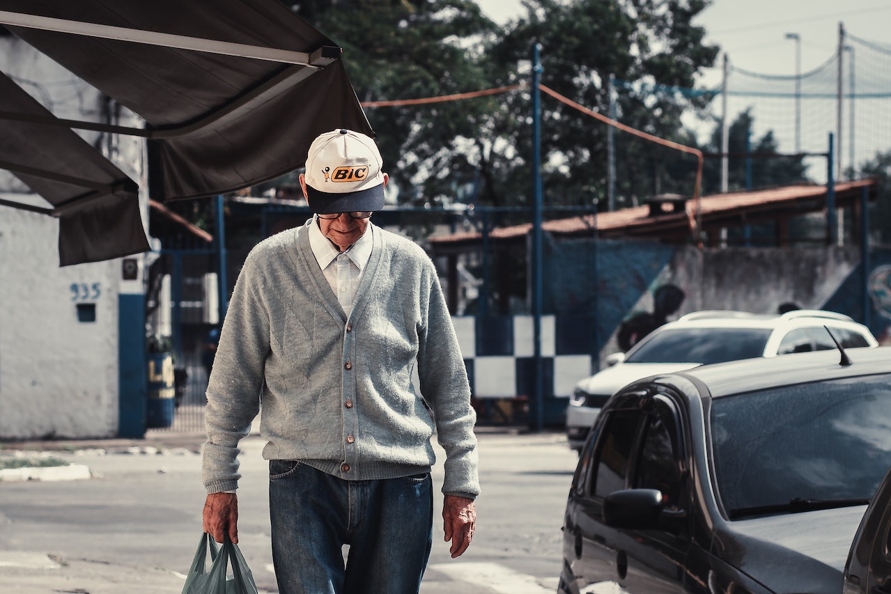 Man in Gray Dress Shirt and Blue Denim Jeans Wearing Hat Standing on Street | Veteran Car Donations
