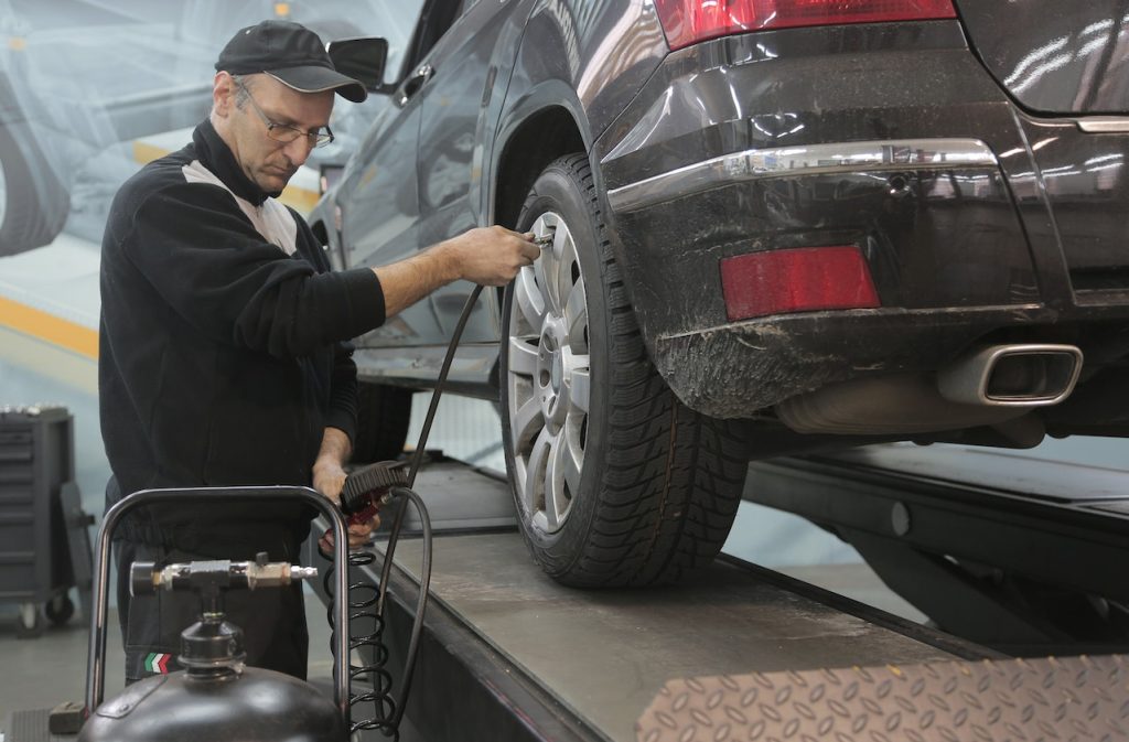 Mechanic pumping up car wheel in modern service garage | Veteran Car Donations
