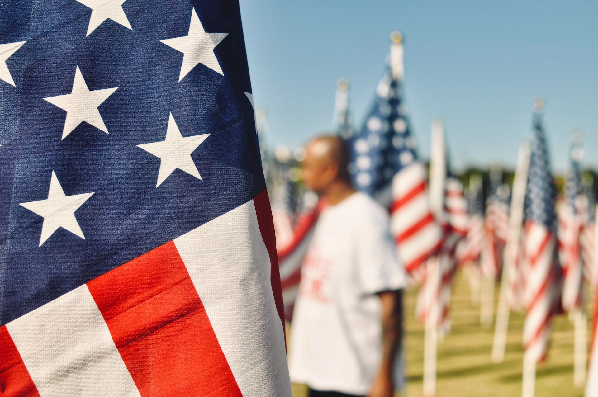 Close up picture of a US flag with a blurry background of a black man and more US flag | Veteran Car Donations
