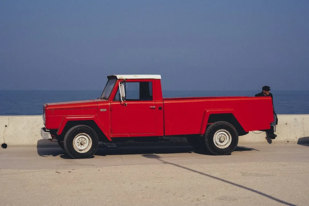 A Man Sitting on the Concrete Railing Near Red Pick Up Truck