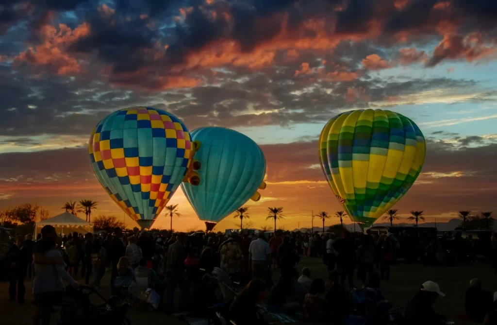A group of people standing around hot air balloons at a festival in Goodyear, Arizona
