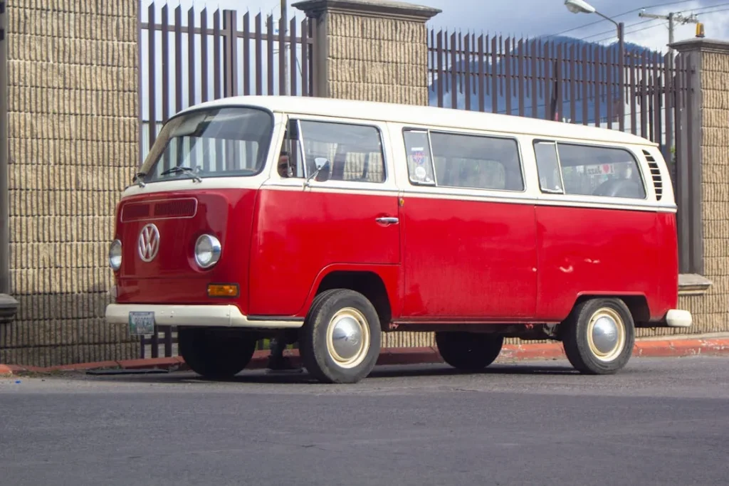 Photo of a red and white Volkswagen bus parked in front of a gate
