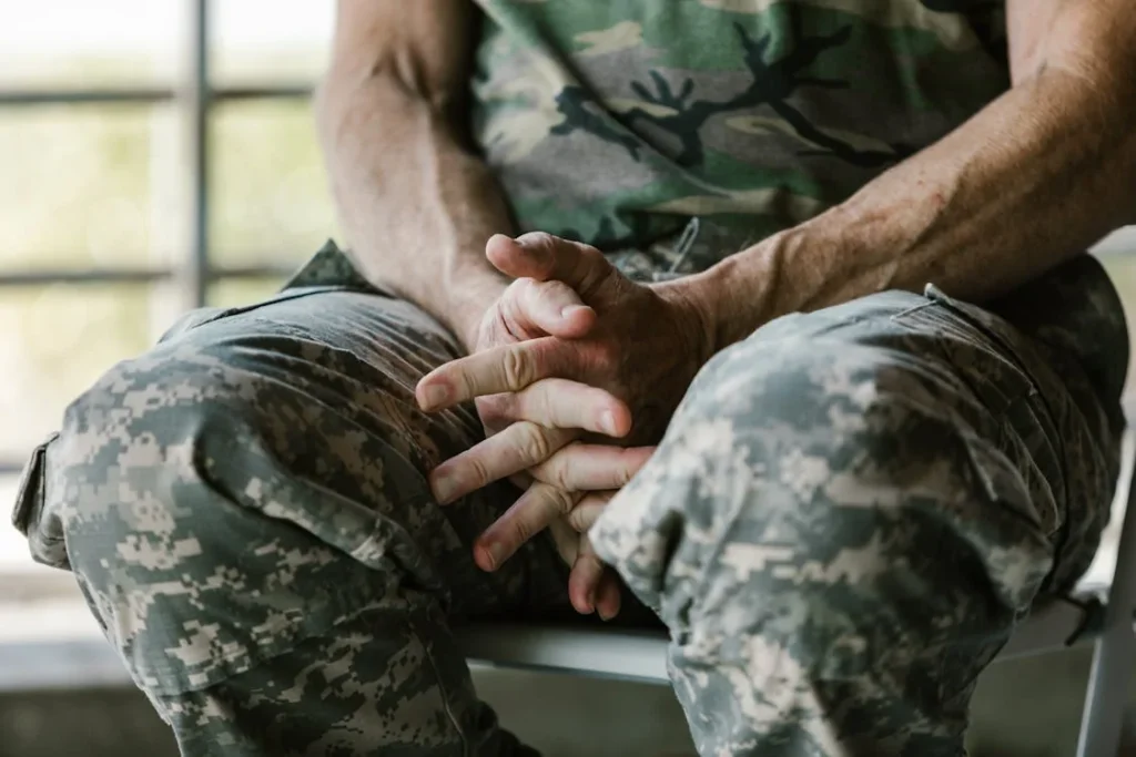 Close-up of a man wearing a green and brown camouflage shirt with hands folded