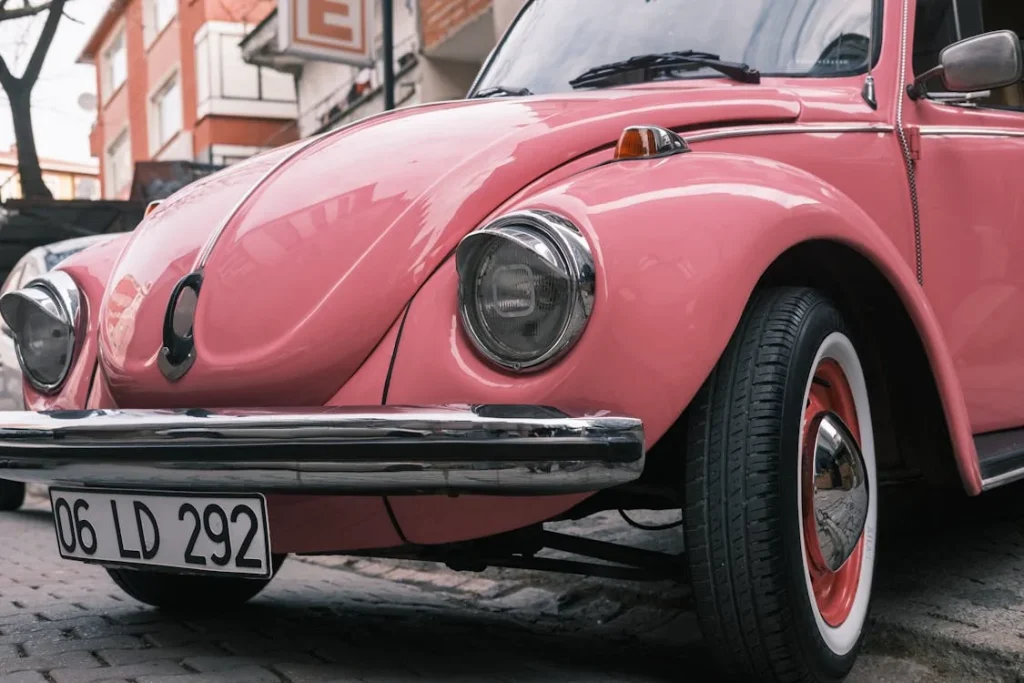 Photograph of a vintage pink Volkswagen Beetle parked on a cobblestone street