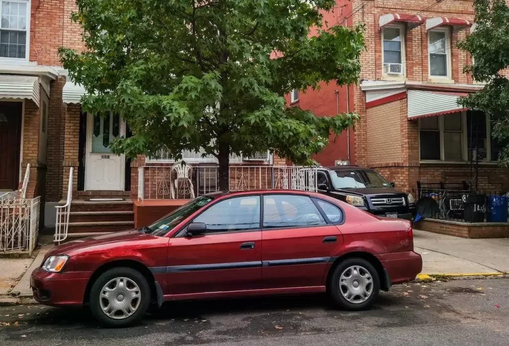 Red sedan parked beside a green tree