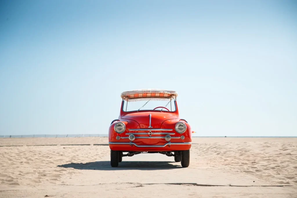 Red vintage car parked on a sandy beach