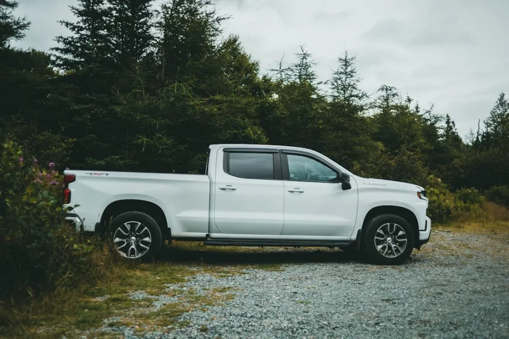 White pickup truck parked beside green trees