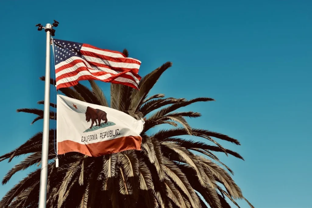American and California flags waving under a blue sky