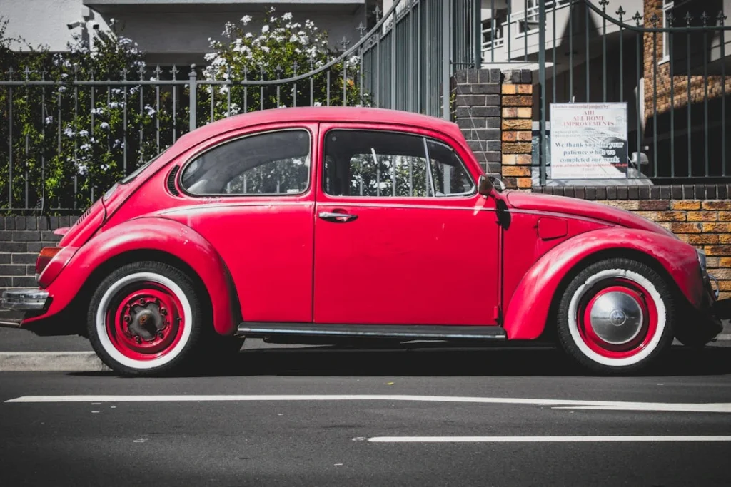 Classic red Volkswagen Beetle parked on an asphalt road in an urban setting