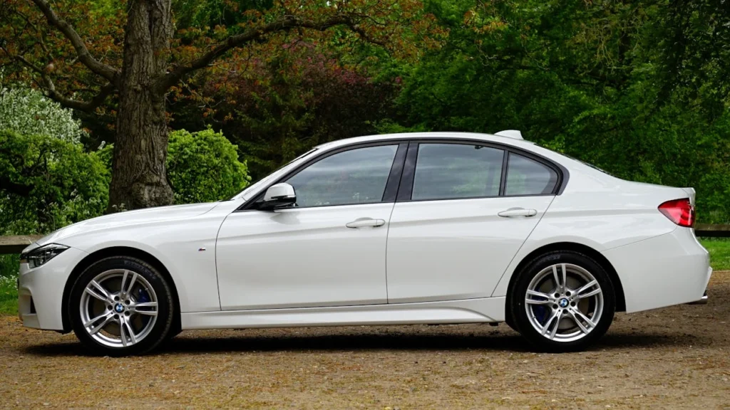 White BMW sedan parked beside trees in a lush outdoor setting